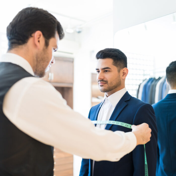 Young salesman doing necessary measurements before giving suit to client at rental store